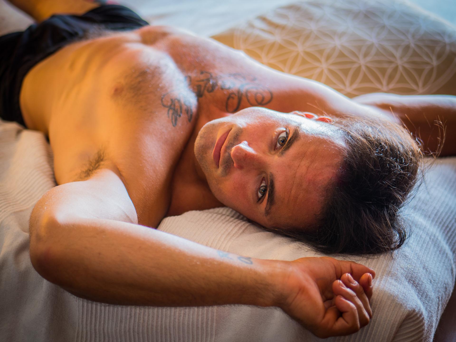 a shirtless man on a bed looking seductively at the camera