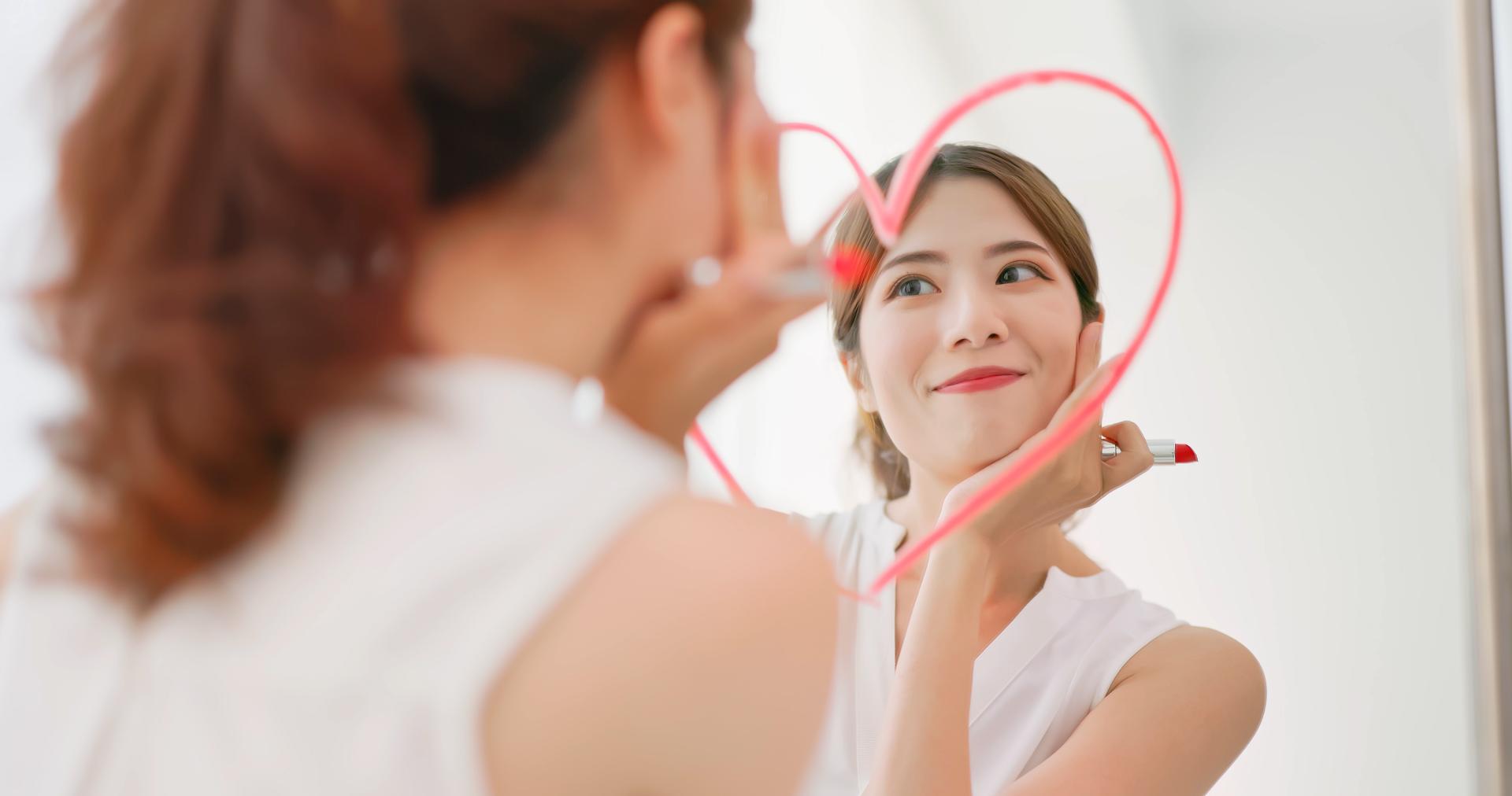 Woman in front of a mirror on which she drew a heart with lipstick Woman in front of a mirror on which she drew a heart with lipstick