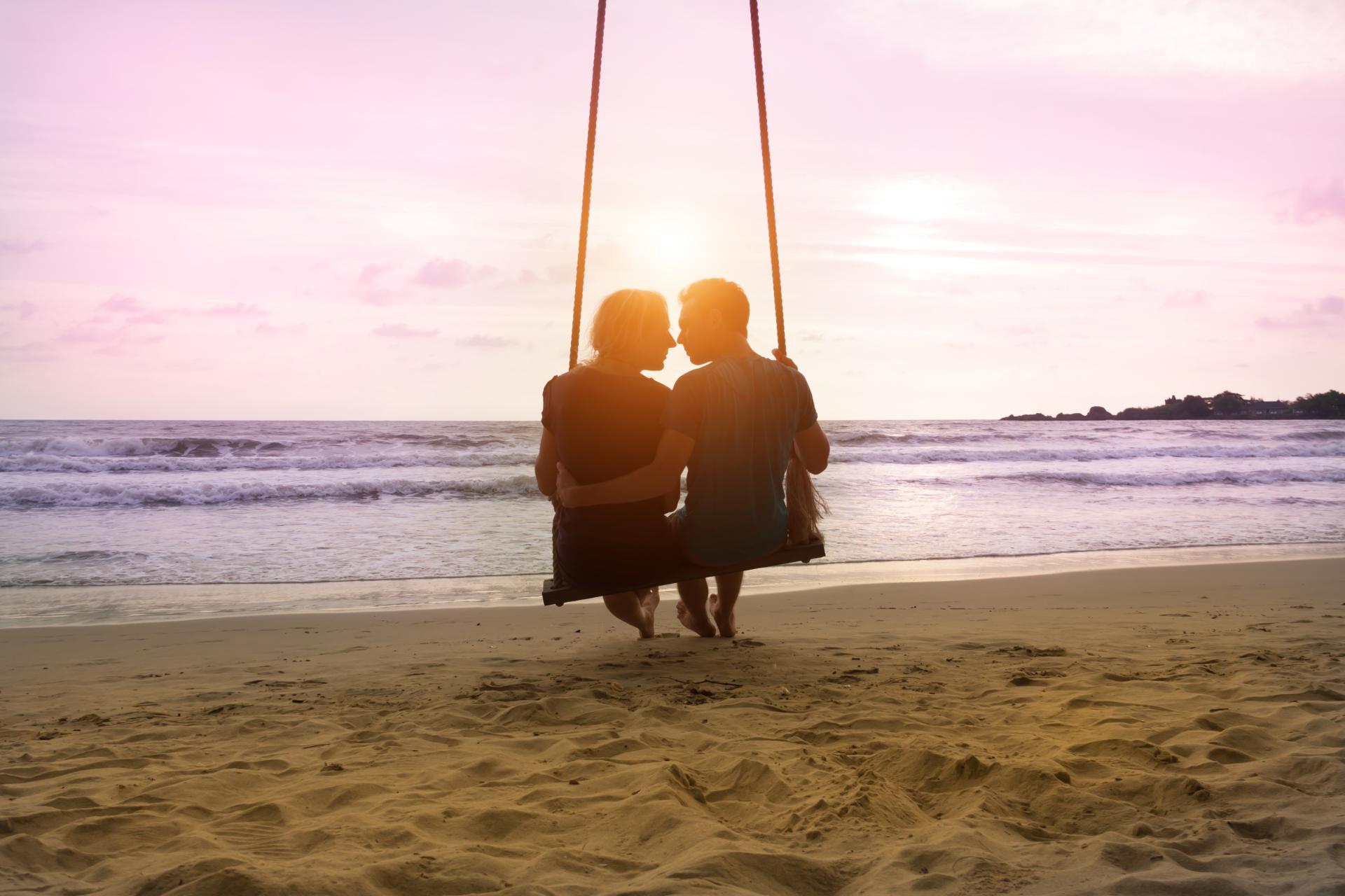 silhouette of a couple about to kiss on a beach swing at sunset silhouette of a couple about to kiss on a beach swing at sunset