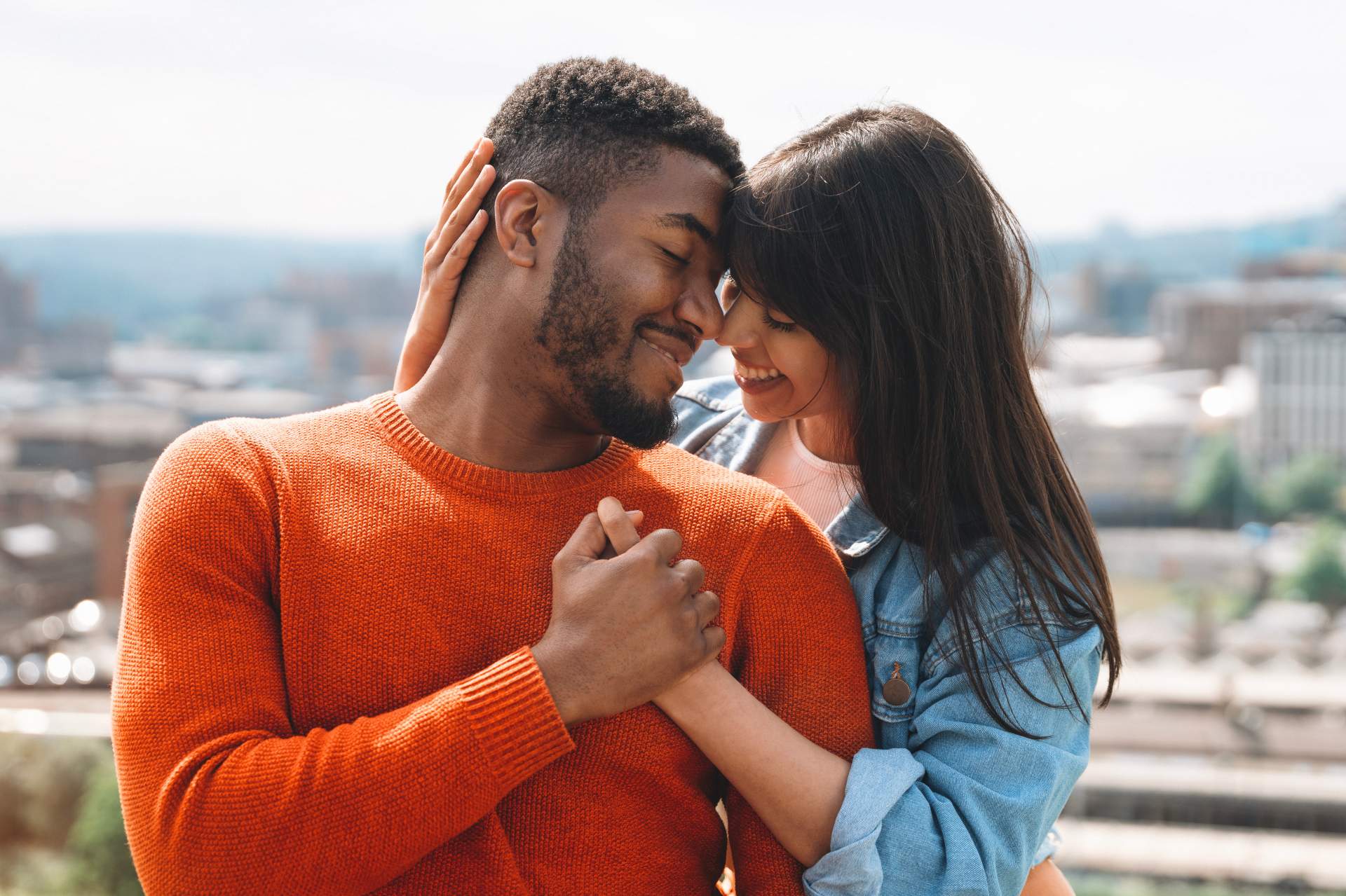 happy loving couple embracing tenderly in front of a blurred daytime cityscape happy loving couple embracing tenderly in front of a blurred daytime cityscape
