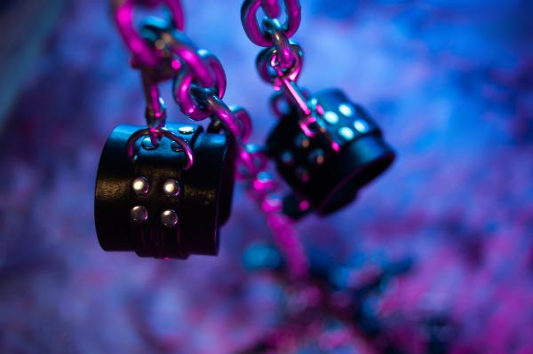 a photo of BDSM leather handcuffs on a metal chain with blue and purple lighting a photo of BDSM leather handcuffs on a metal chain with blue and purple lighting