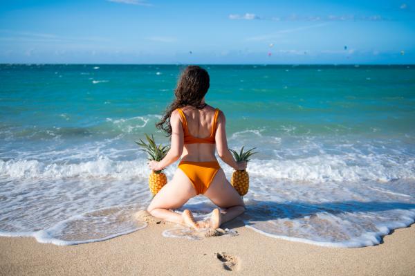 A photo of a woman holding pineapples in each hand kneeling on a Jamaican beach A photo of a woman holding pineapples in each hand kneeling on a Jamaican beach