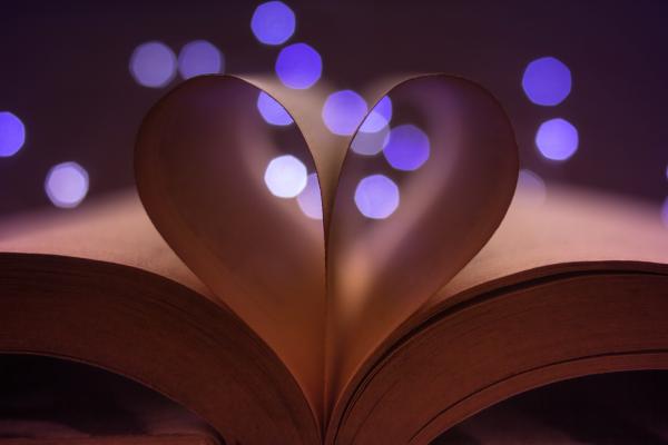 a photo of an open book with pages folded in to form a heart over purple background lights a photo of an open book with pages folded in to form a heart over purple background lights