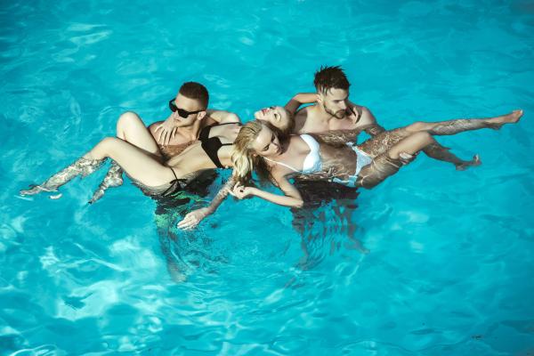 two couples in a pool with the women resting their heads on each others shoulders two couples in a pool with the women resting their heads on each others shoulders