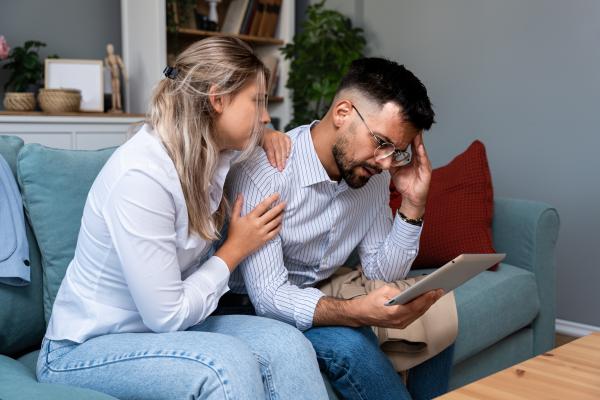 overwhelmed couple looking at a tablet while sitting on the couch overwhelmed couple looking at a tablet while sitting on the couch