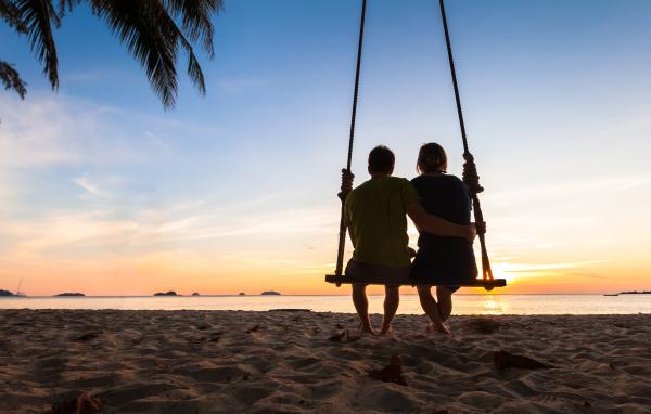 silhouette of a couple sitting together on a beach swing facing the ocean silhouette of a couple sitting together on a beach swing facing the ocean