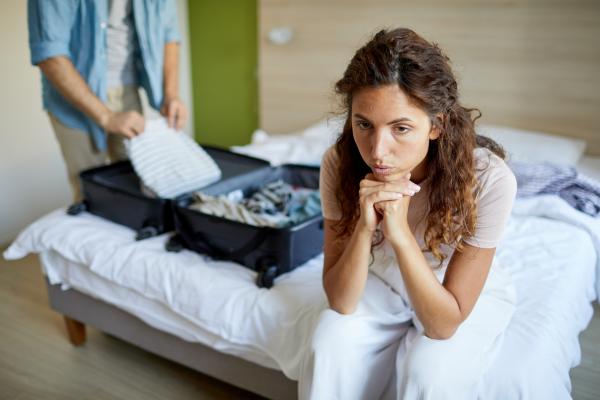 woman disappointed in male partner as he packs a suitcase behind her woman disappointed in male partner as he packs a suitcase behind her