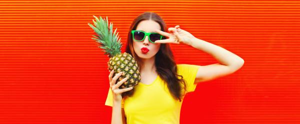 woman wearing green sunglasses over a red background holding a pineapple and making a peace sign woman wearing green sunglasses over a red background holding a pineapple and making a peace sign