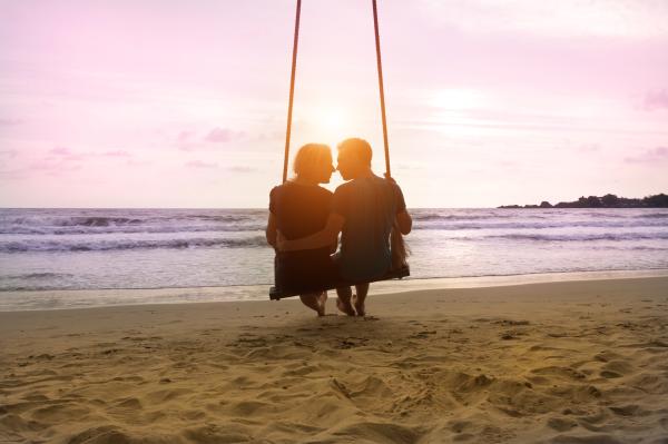 silhouette of a couple about to kiss on a beach swing at sunset silhouette of a couple about to kiss on a beach swing at sunset