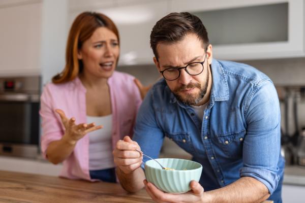 Woman gesturing and pleading to a man looking away from her in a kitchen Woman gesturing and pleading to a man looking away from her in a kitchen