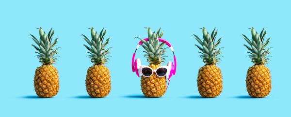 Row of fresh pineapples with one wearing sunglasses and headphones over a blue background Row of fresh pineapples with one wearing sunglasses and headphones over a blue background