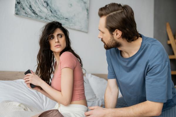 Woman hiding her phone from her boyfriend who is looking at her intently Woman hiding her phone from her boyfriend who is looking at her intently