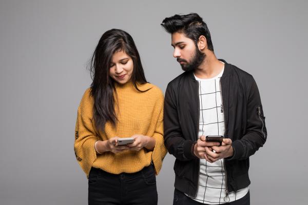 Couple holding their mobile phones with the man looking suspiciously at the woman's phone Couple holding their mobile phones with the man looking suspiciously at the woman's phone