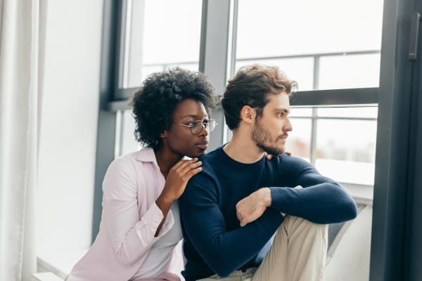 Woman comforting a man looking out the window with a sad expression Woman comforting a man looking out the window with a sad expression
