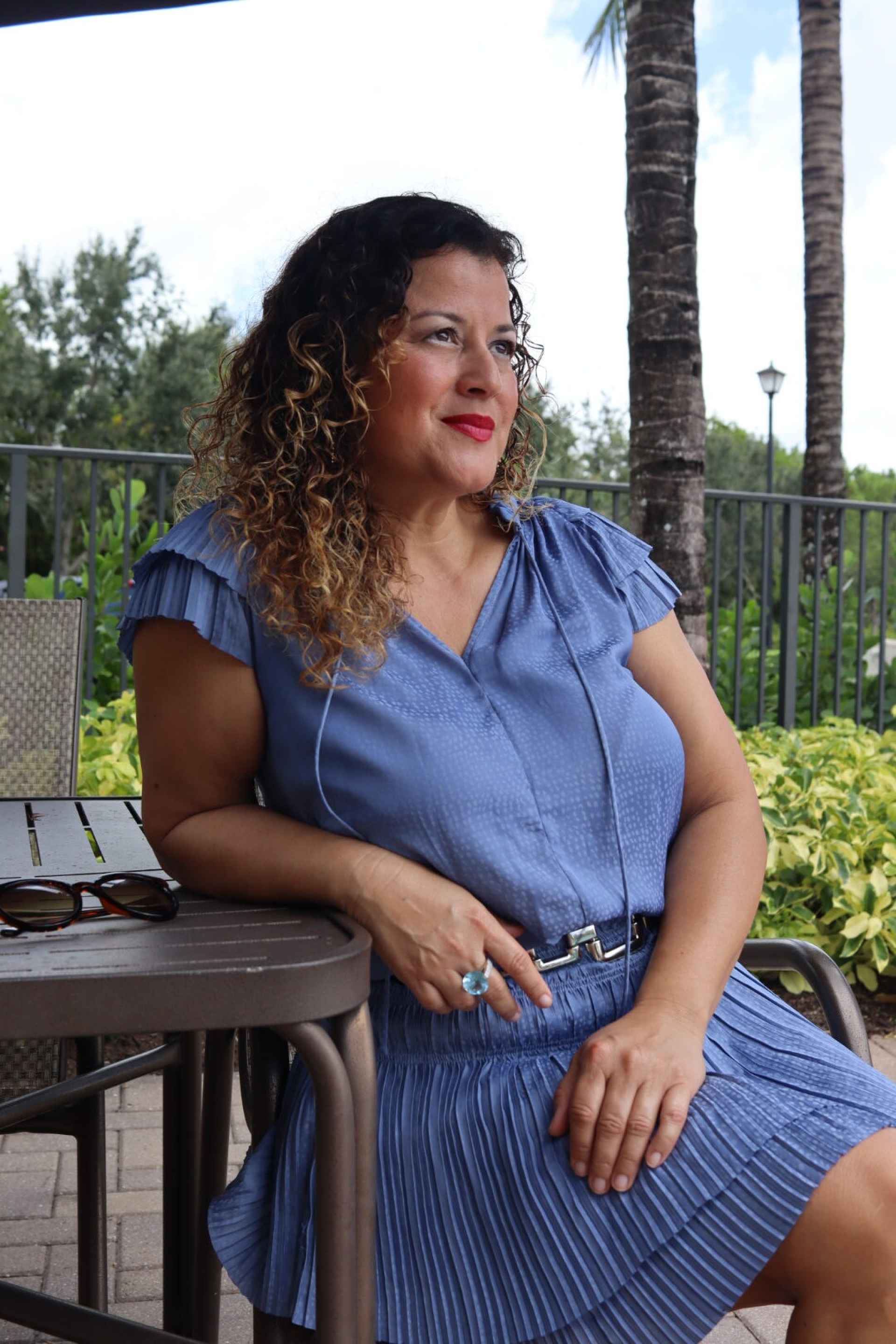 woman with dark curly hair in a blue outfit sitting outside during daytime