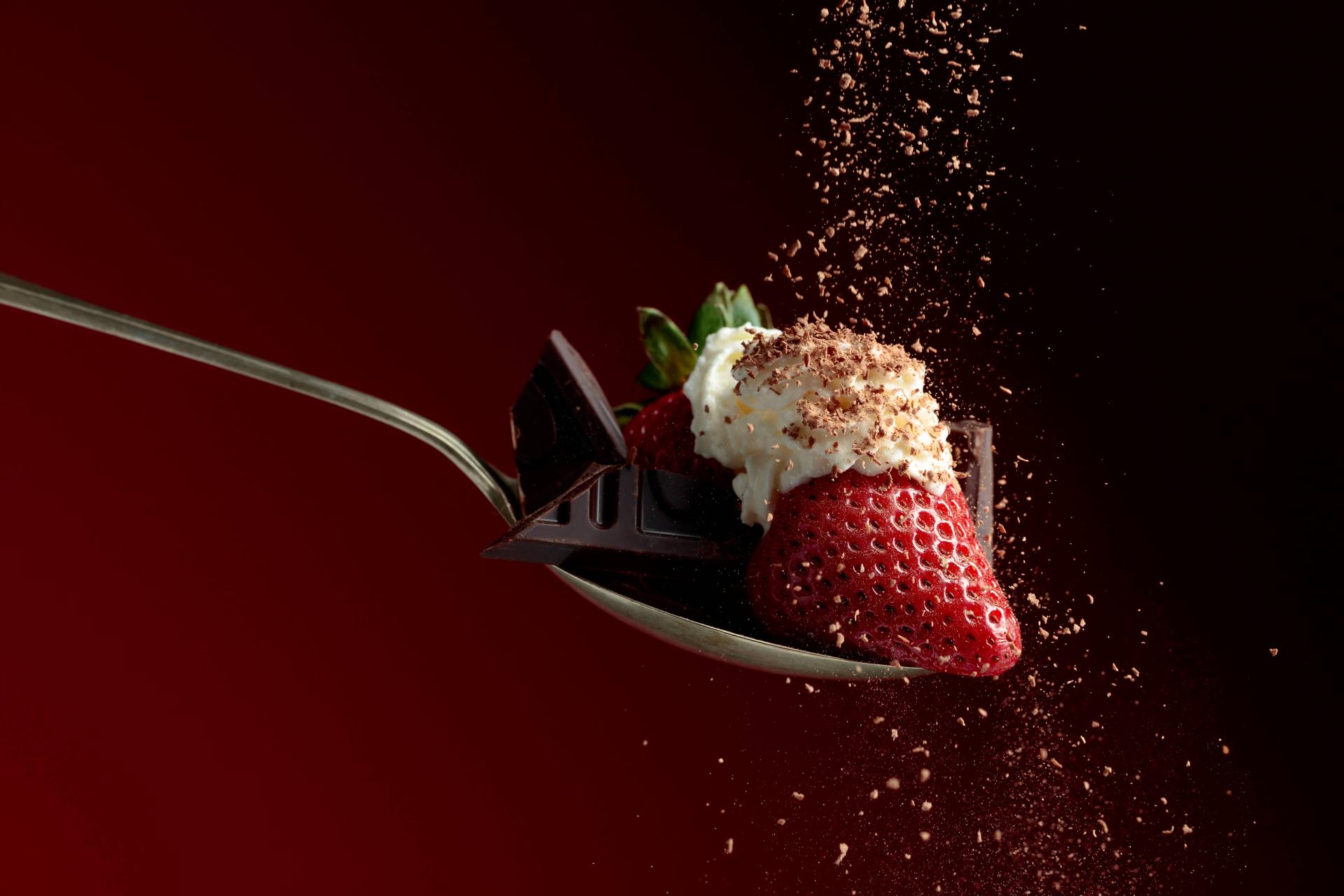 a strawberry with chocolate and whipped cream over a red background