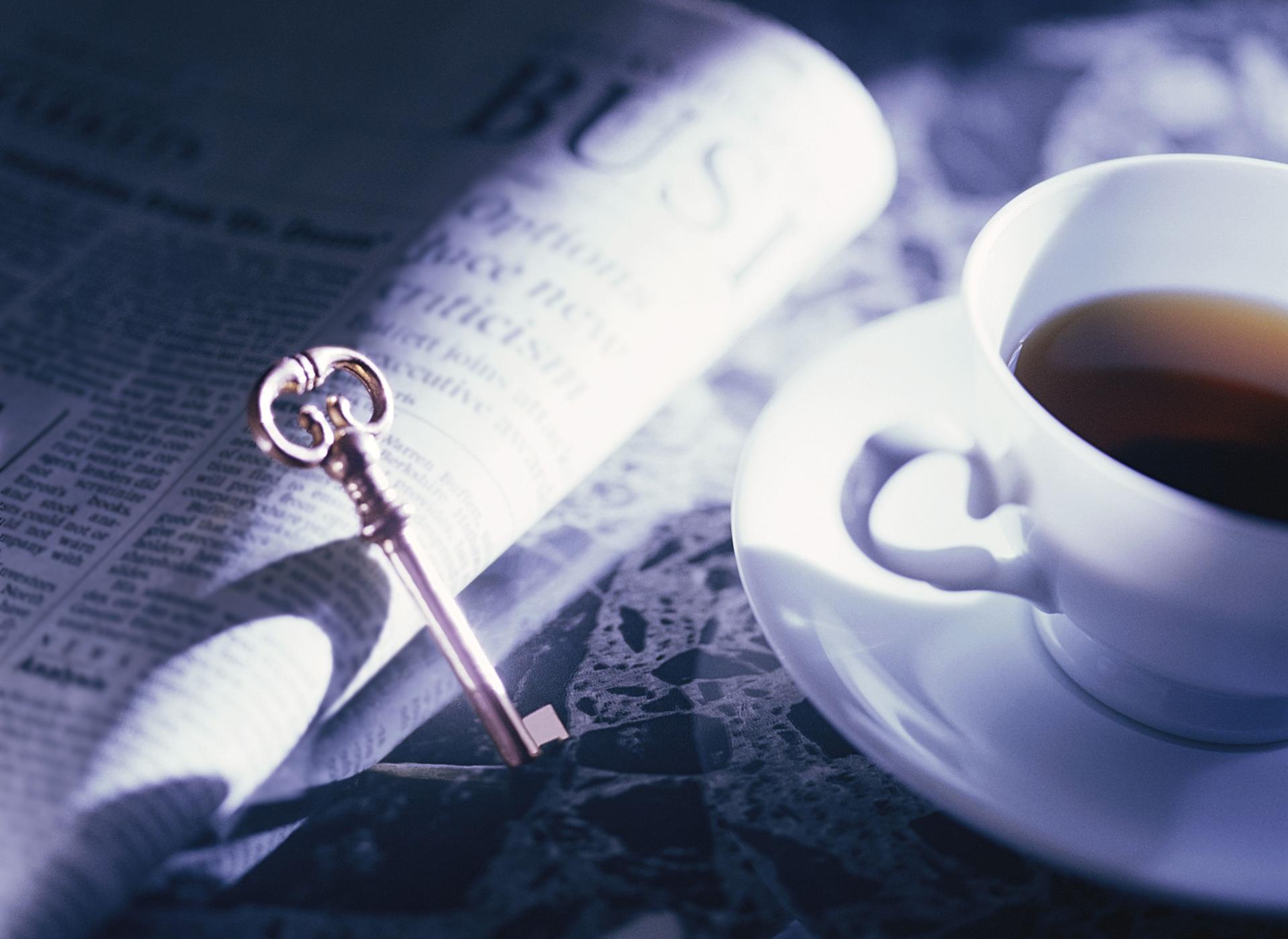 closeup of a key leaning against an opened newspaper page next to a coffee cup