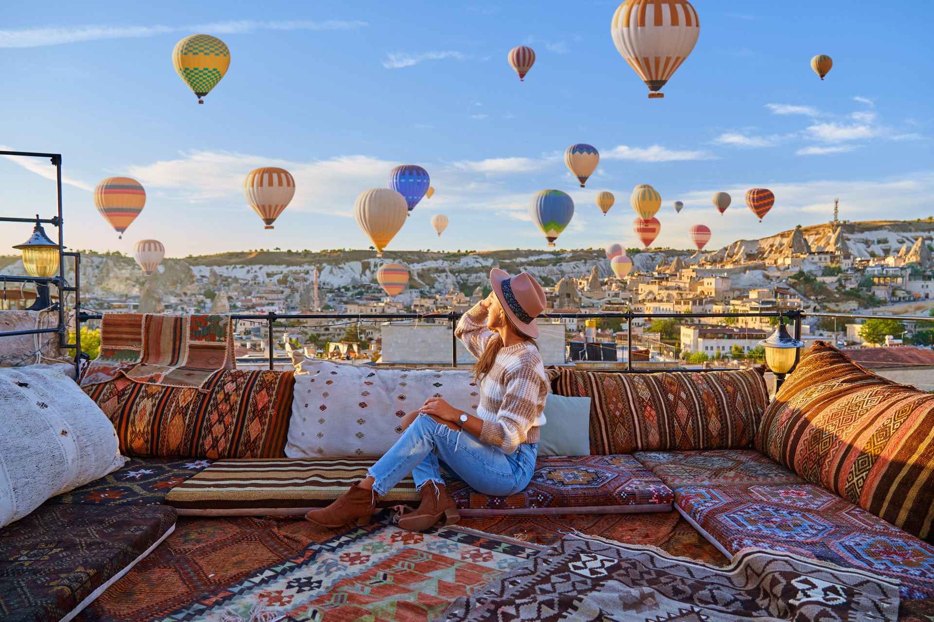 woman on rugs and pillows on a rooftop looking at air balloons