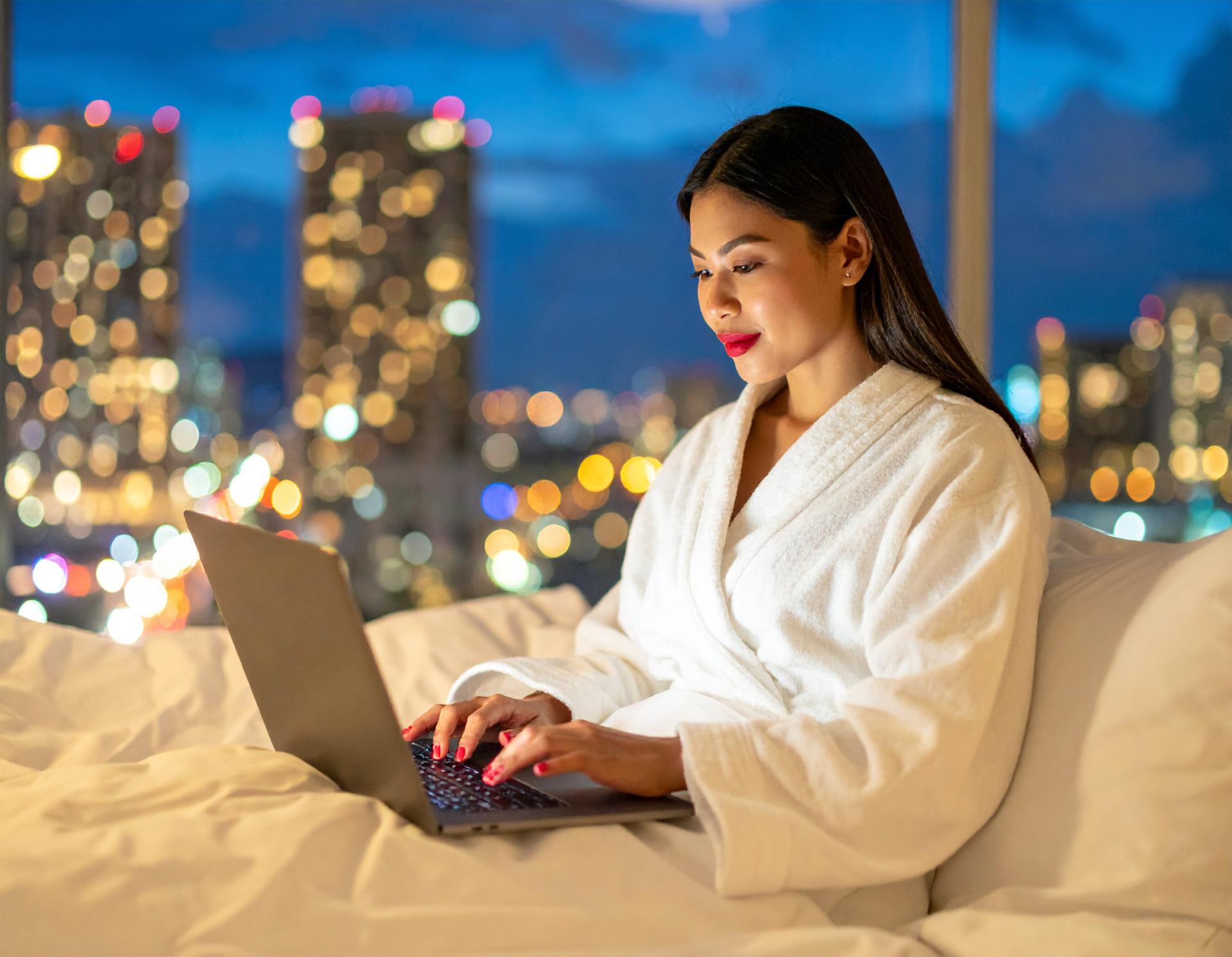woman wearing red lipstick and a robe typing on her laptop in bed at night woman wearing red lipstick and a robe typing on her laptop in bed at night