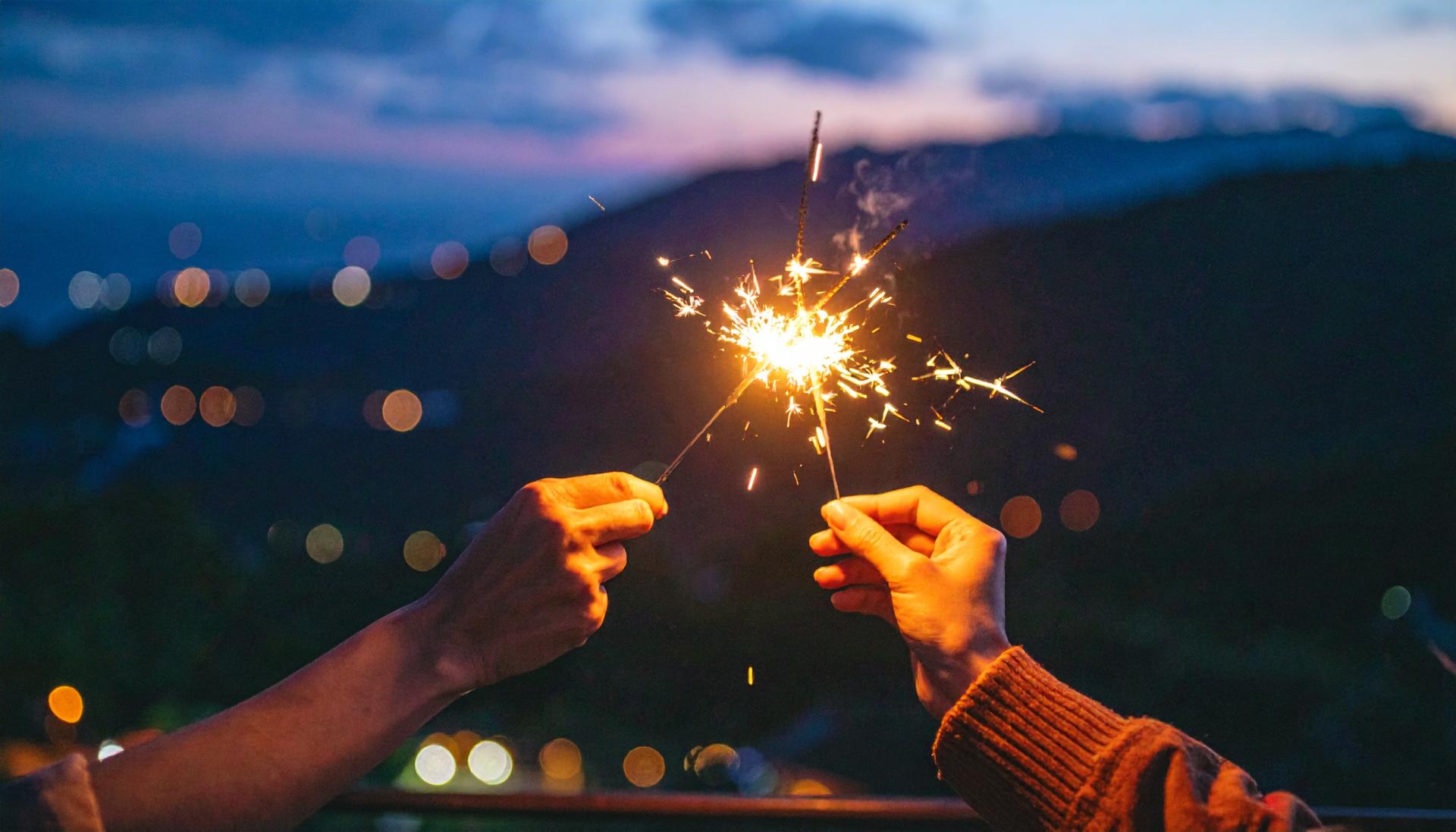 two hands holding sparklers at night