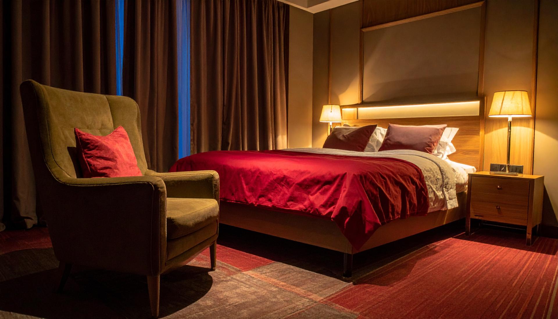 dimly lit hotel room with an accent chair and bed with red sheets