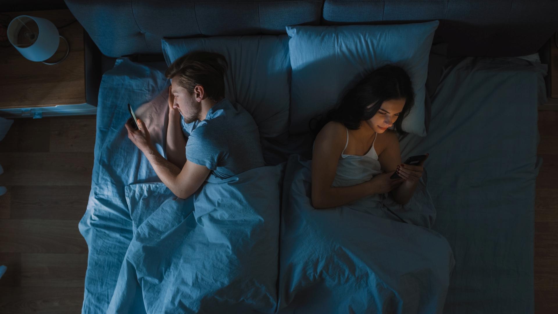 couple on their phones facing away from each other in bed at night