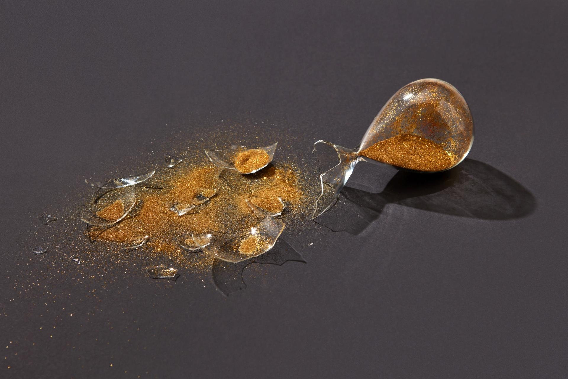 broken hourglass with gold sand spilled over a dark background