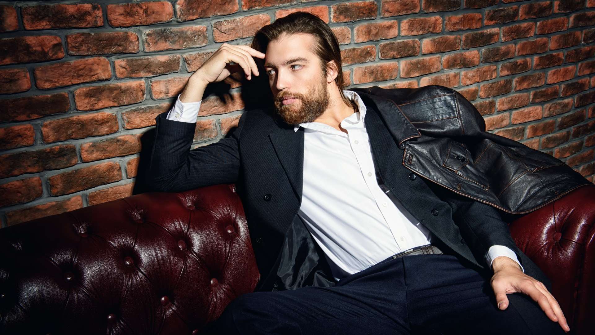 contemplative man in a suit and leather jacket on a leather sofa