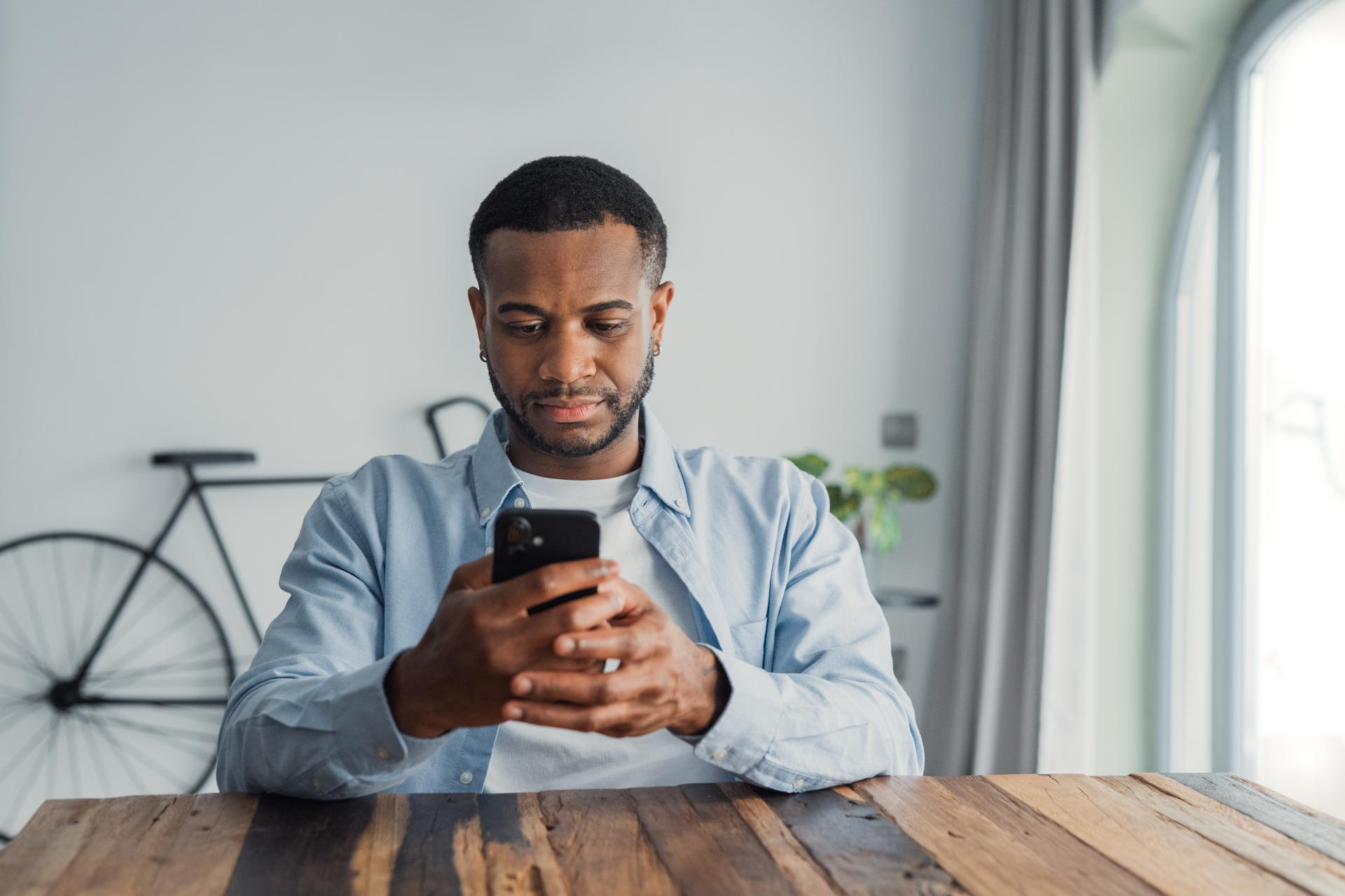 a man sitting at a table checking his phone and looking anxious