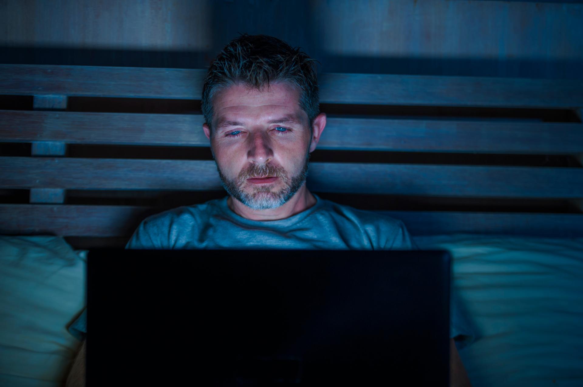 a man wearing a blue shirt appearing exhausted looking at something on his laptop