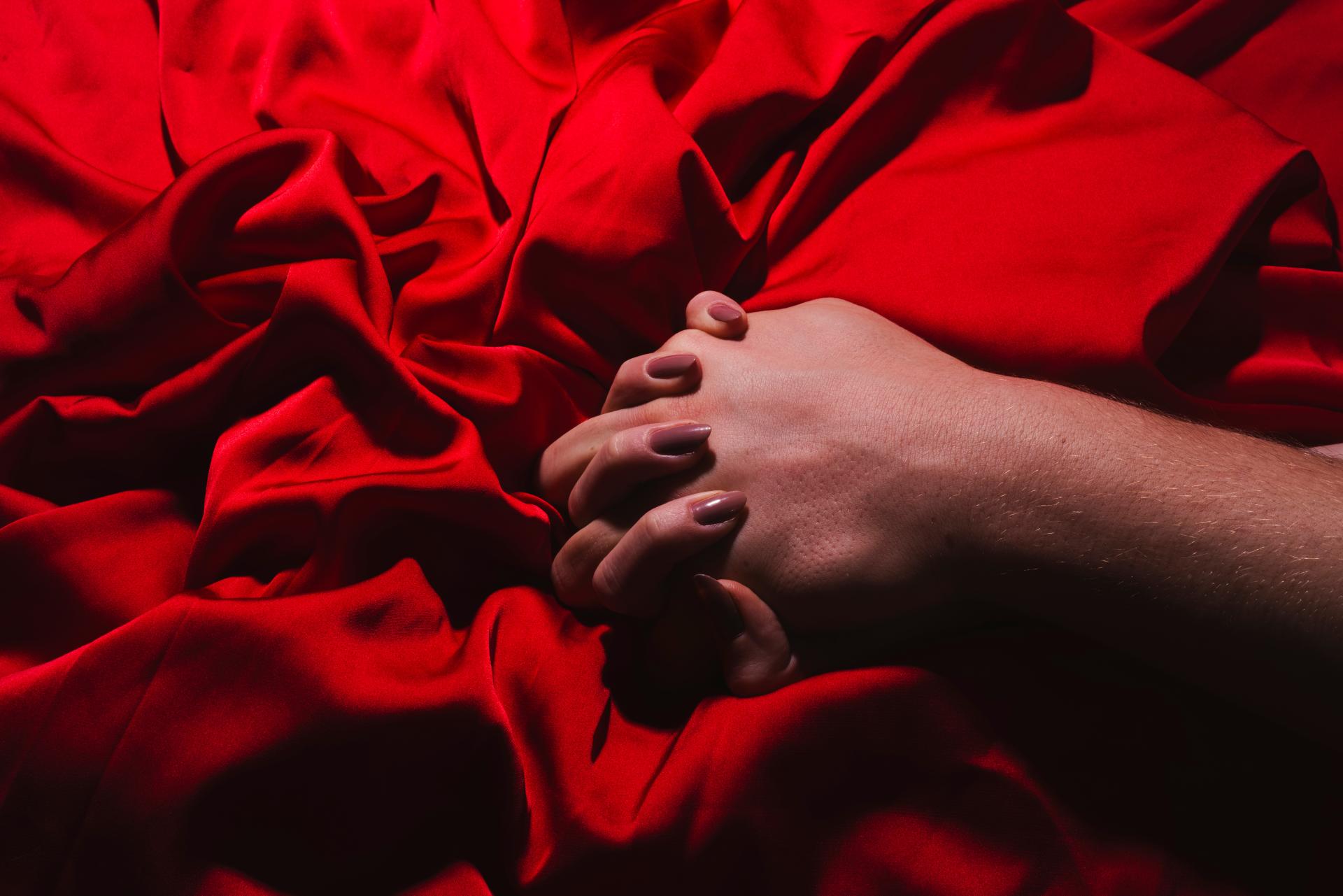two hands holding each other against a red silk sheet