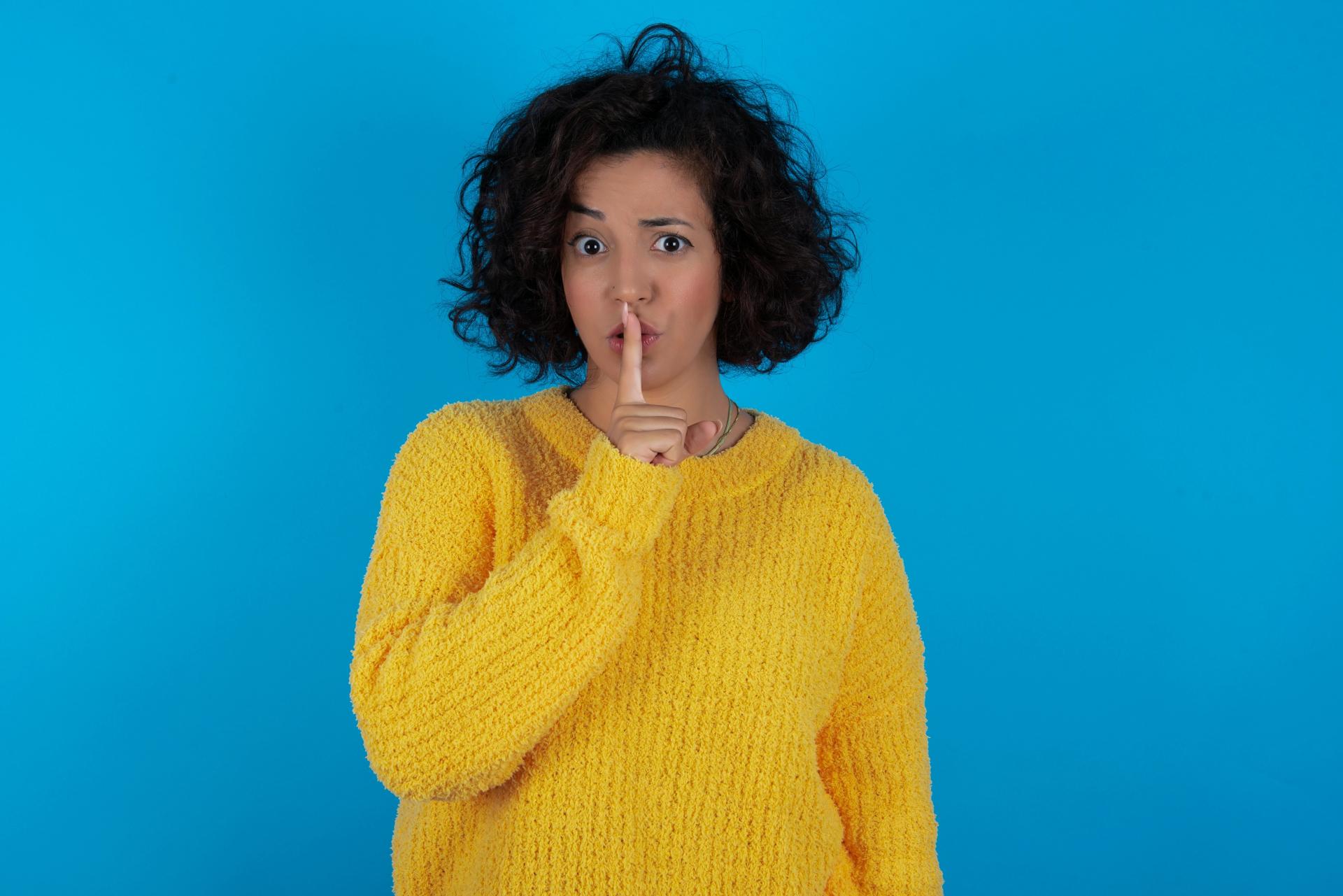 a woman wearing a yellow shirt with one finger over her lips