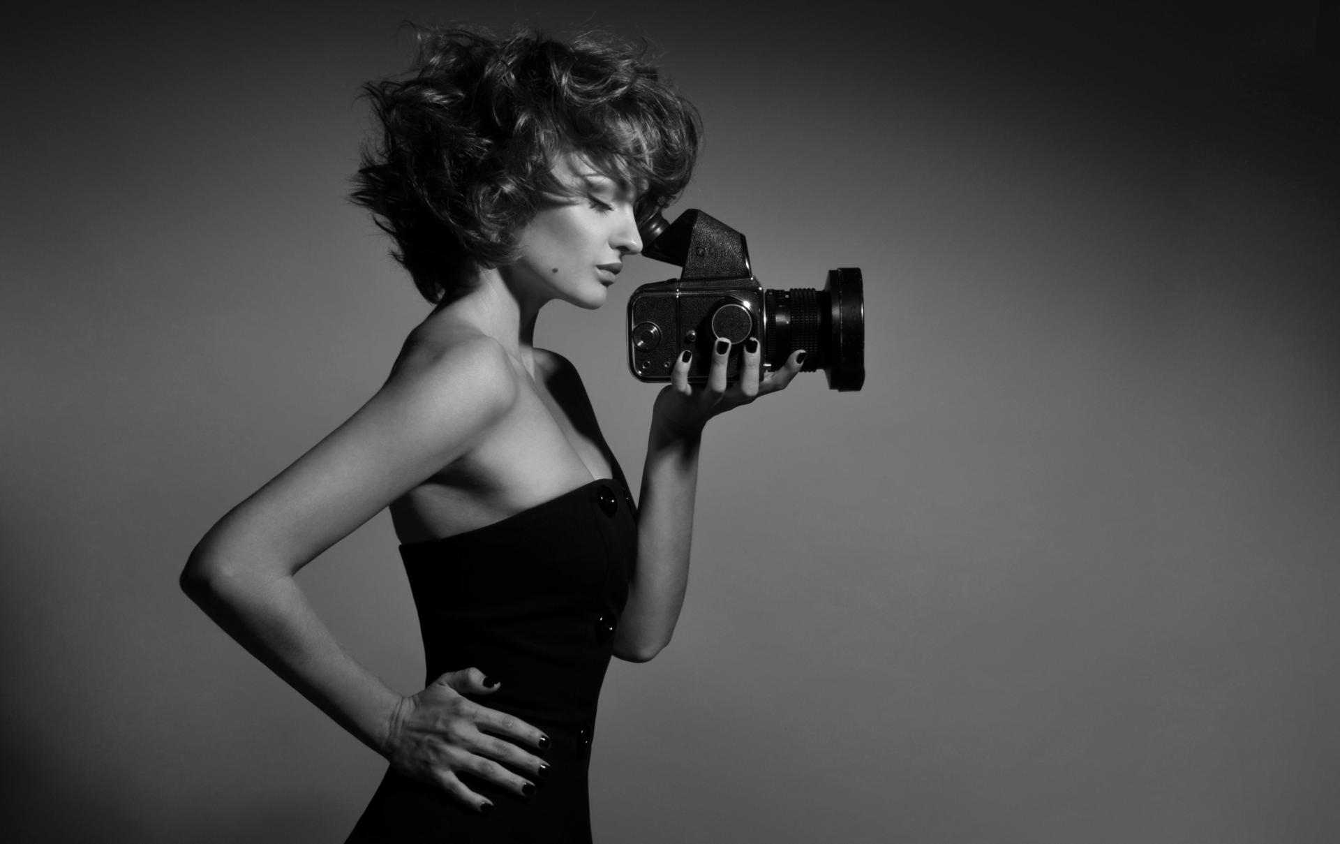 black and white photo of a woman wearing a black tube top holding a camera