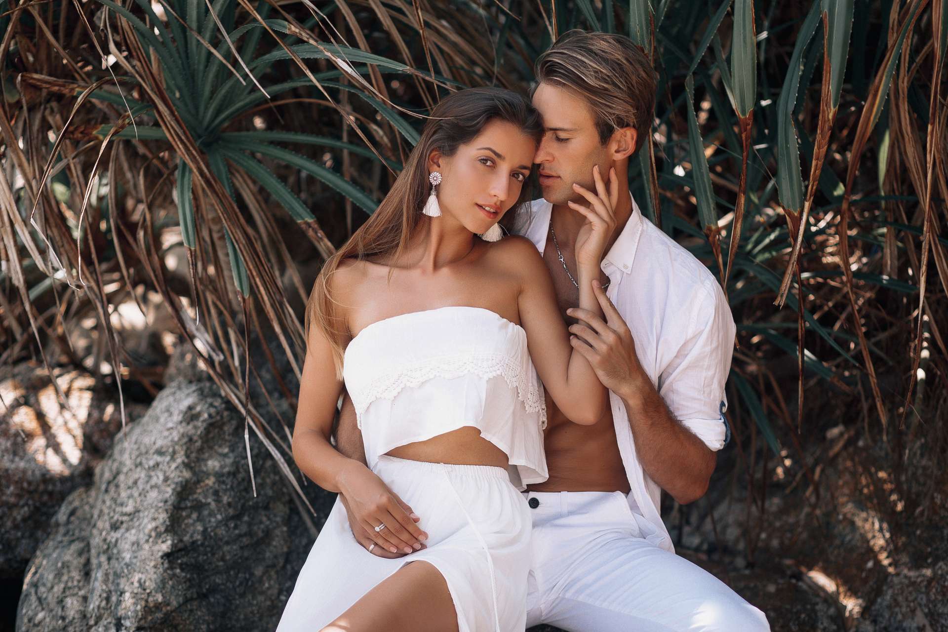 a man and woman dressed in white with palm trees in the background