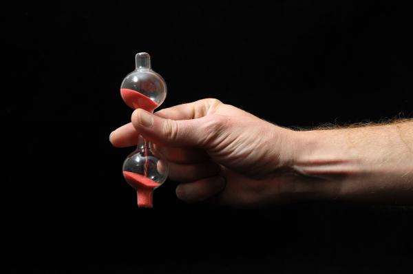 man's hand holding a small red sand timer over a black background man's hand holding a small red sand timer over a black background