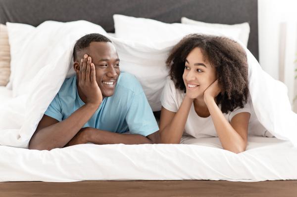 smiling couple in t shirts looking at each other under a white blanket smiling couple in t shirts looking at each other under a white blanket