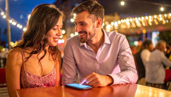 Happy couple on a date looking at a cell phone on the table Happy couple on a date looking at a cell phone on the table