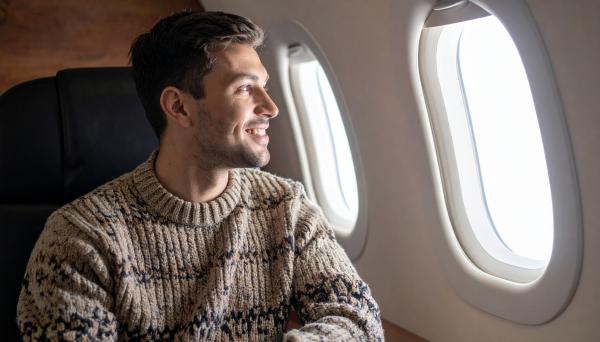 Happy man in a sweater looking out the window on an airplane