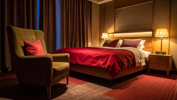 dimly lit hotel room with an accent chair and bed with red sheets
