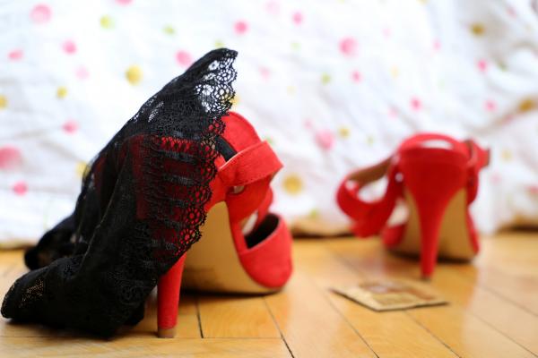 a bedroom floor with red heels and black lingerie and a wrapped condom