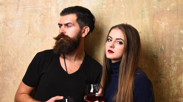 unamused couple wearing black and holding glasses of wine
