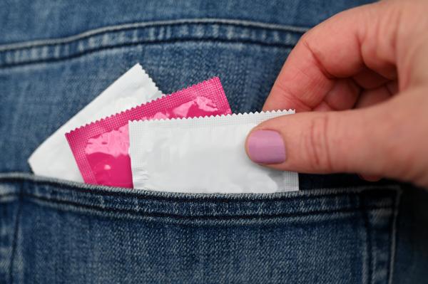 woman grabbing a condom out of the back pocket of a pair of jeans