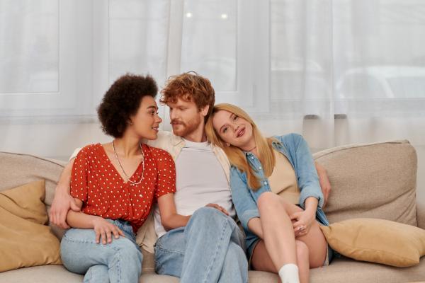 two smiling women on either side of a man all snuggling on a couch