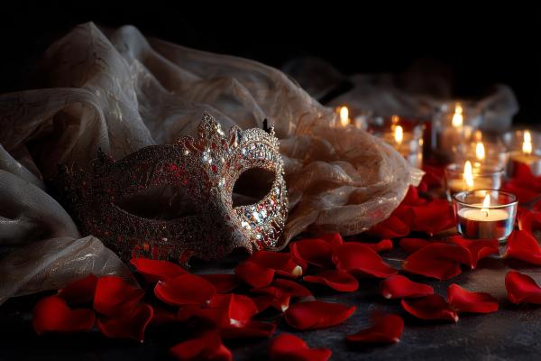elegant jeweled mask resting on a bed of red rose petals with candles in the background