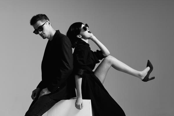 black and white picture of couple sitting back to back dressed in black wearing sunglasses