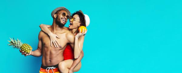 a couple in swimwear embracing and laughing while holding a pineapple
