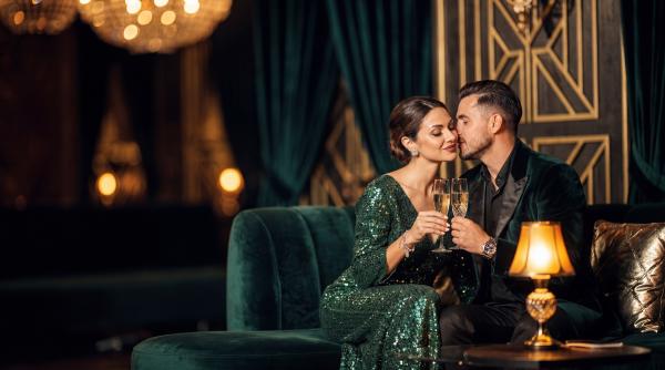 woman in green dress man dressed in black sitting close and holding champagne