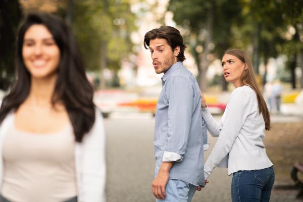 a man checking out a woman walking by while is girlfriend gives him a jealous look