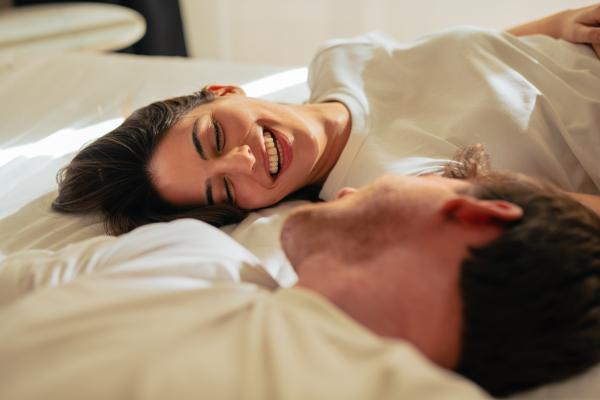 a couple wearing white t-shirts talking happily in bed
