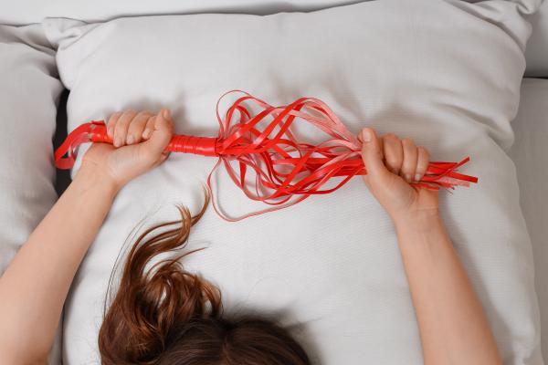 two hands holding a red whip over a white pillow